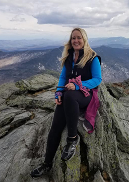 Selena Paquette, Business Manager for Integrity Awnings posing for a photo sitting on a mountain peak.